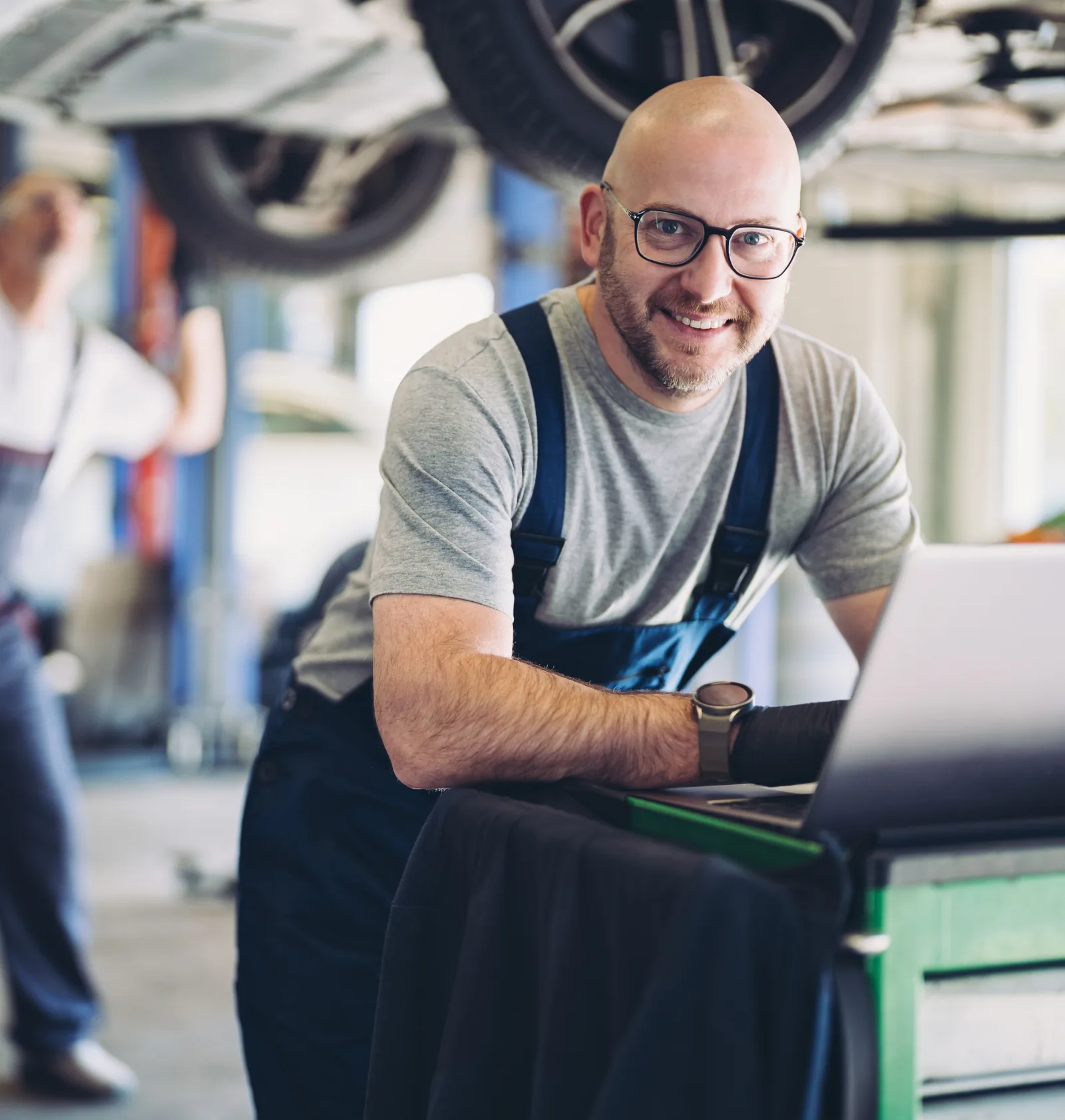 An auto repair shop owner at his laptop beneath a car on a lift