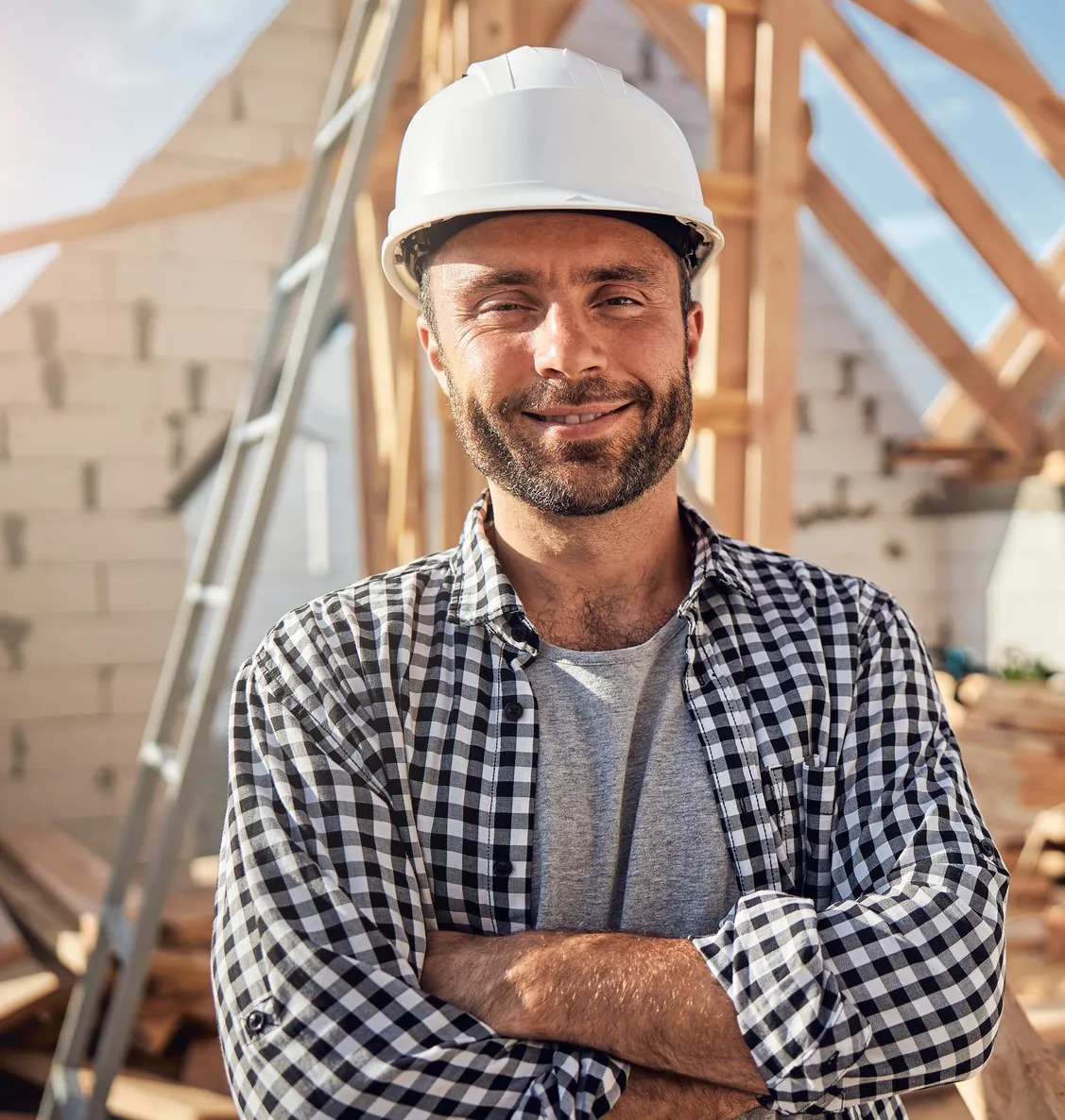 Contractor in a hard hat and flannel shirt standing at a framed construction site
