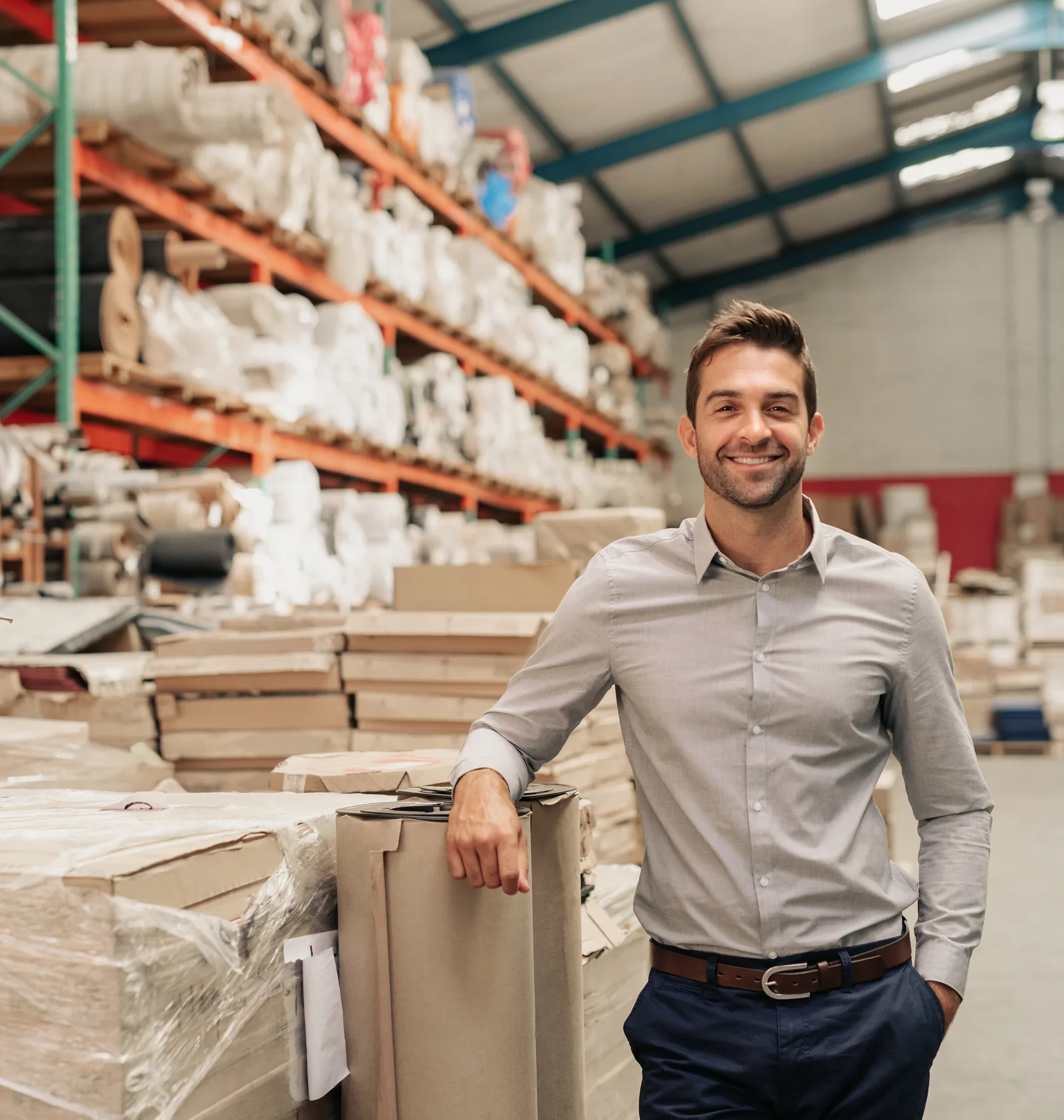 A manufacturing business owner standing in his production warehouse among stacked materials