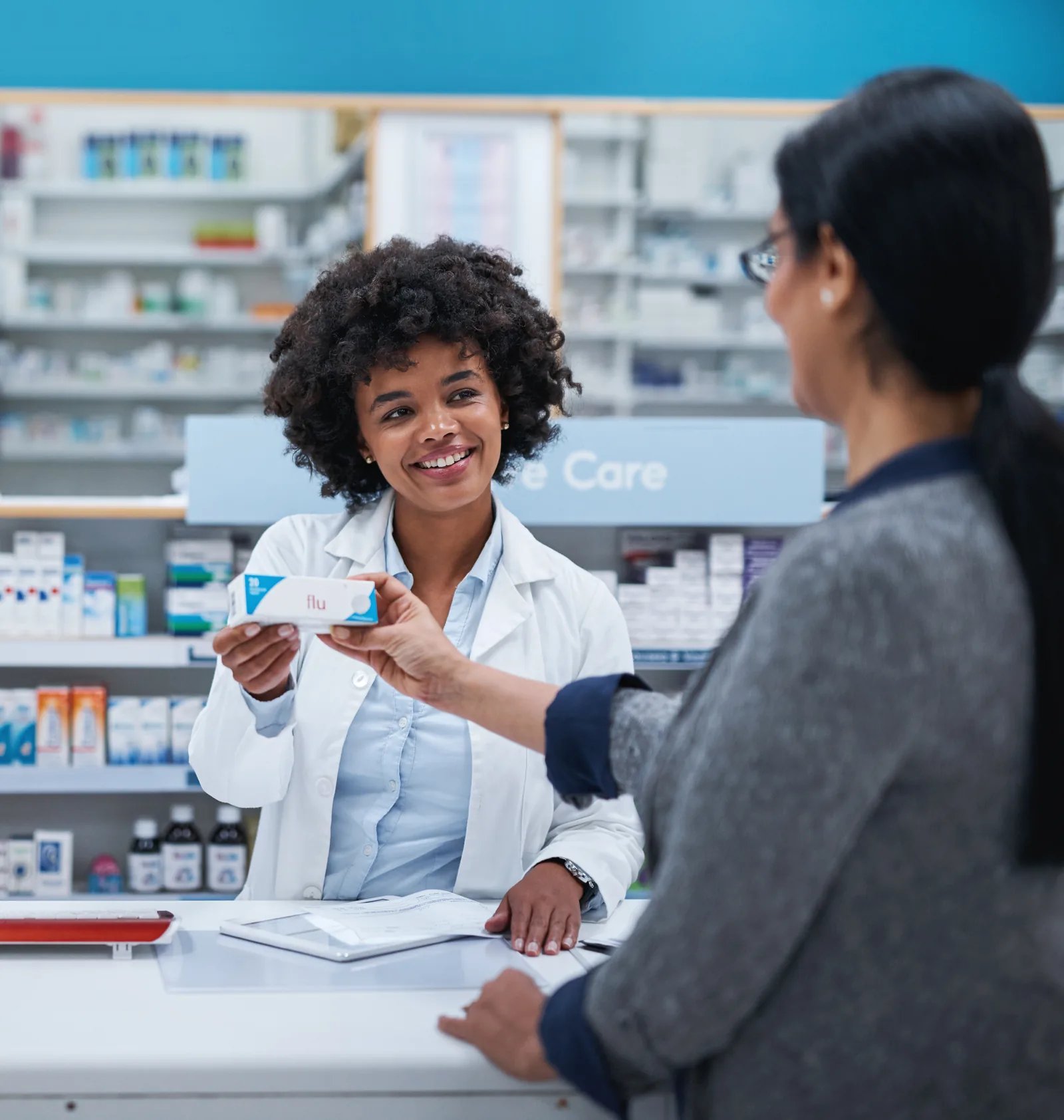 Pharmacist handing a customer a medication box across the pharmacy counter