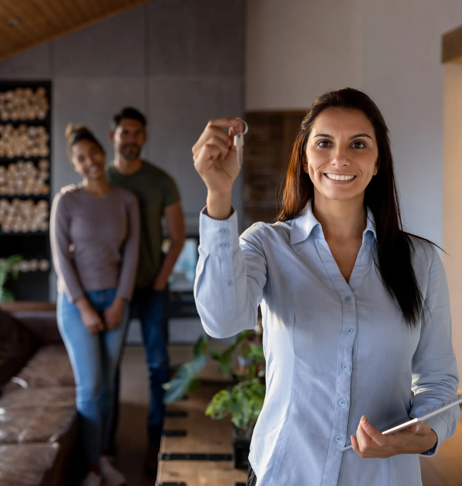 A real estate agent holding up house keys with new homeowners in the background