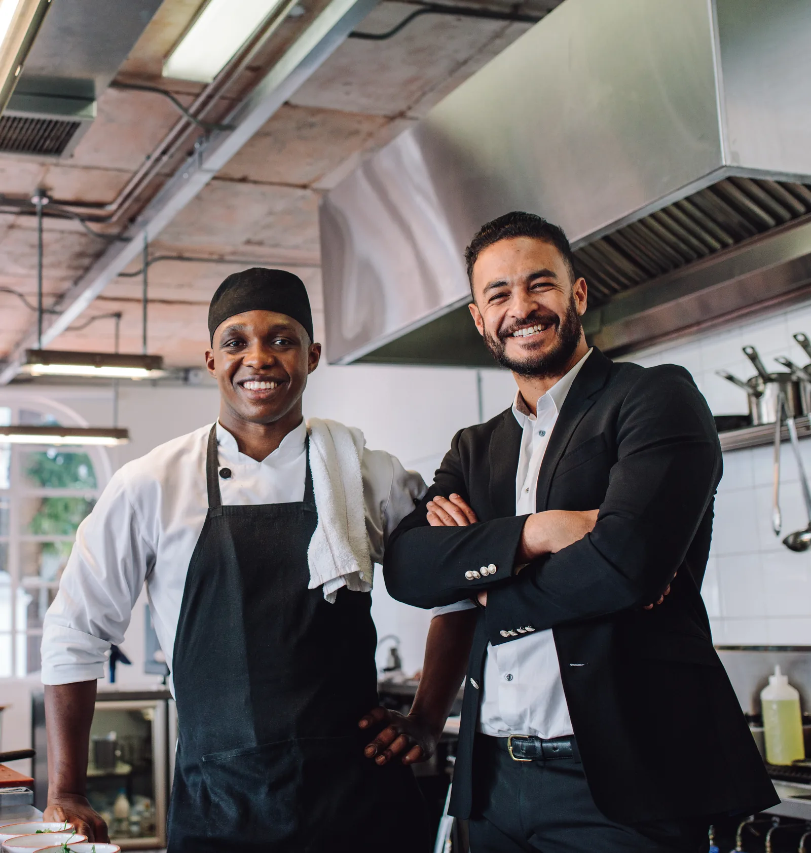 A chef and restaurant owner standing together in a commercial kitchen