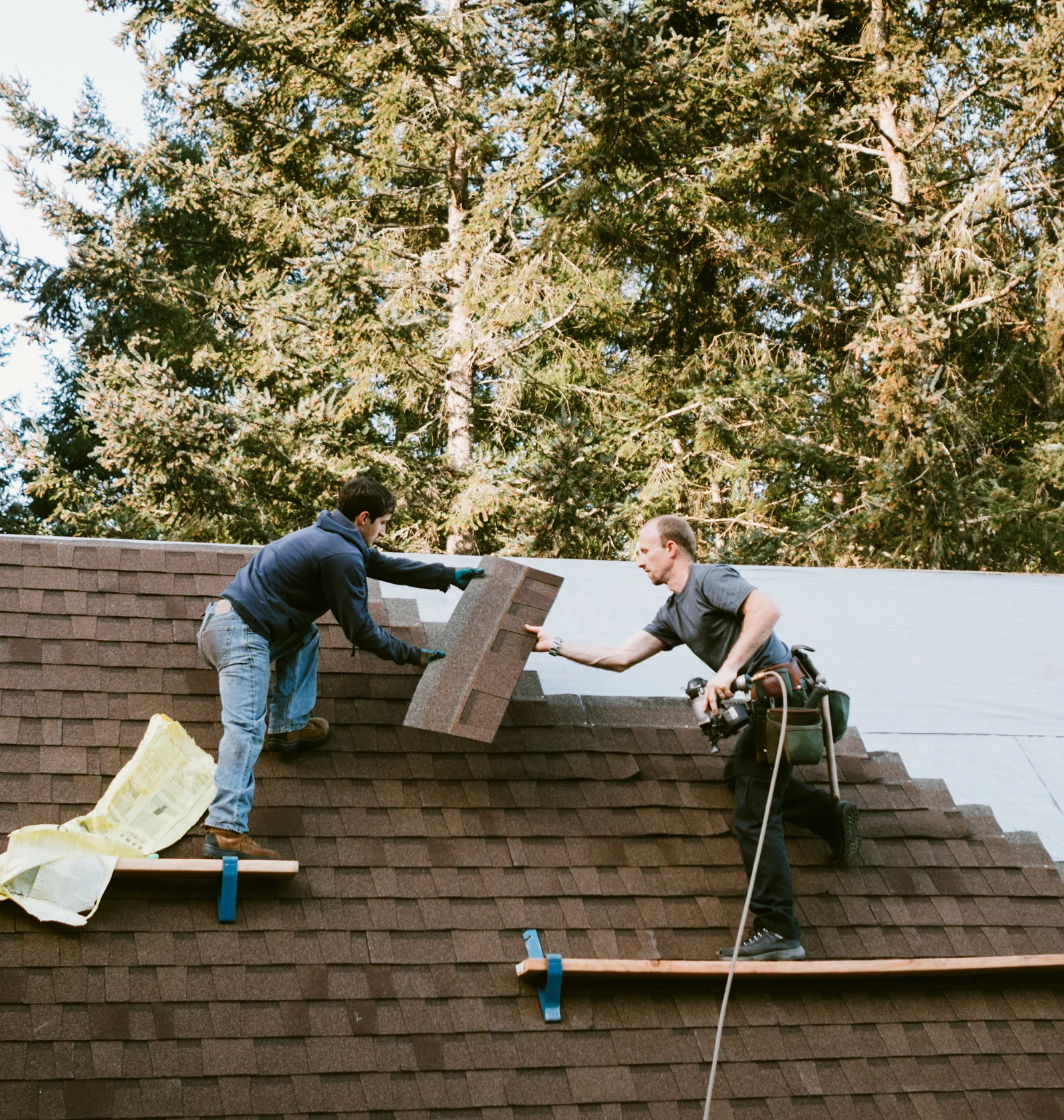 Two roofers installing asphalt shingles on a pitched roof